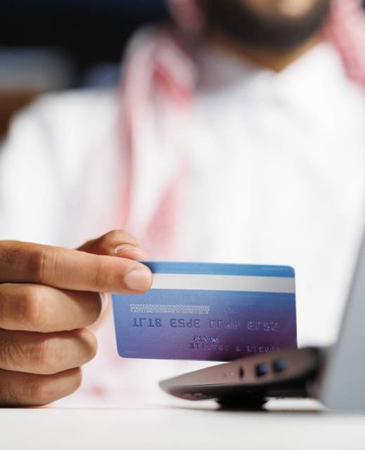 Focused Arab businessman at a modern desk, engrossed in efficient online work. Using wireless technology, he types, researches and shops securely with a credit card.
